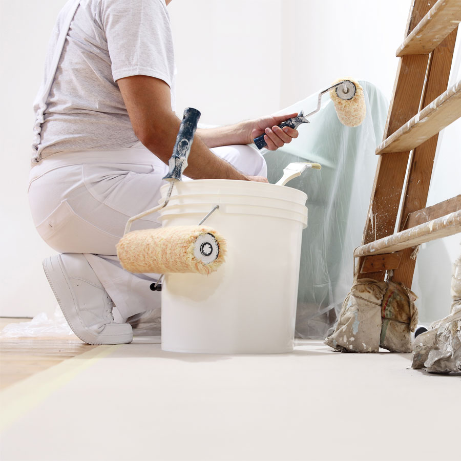 Decorator in white overalls kneeling and painting a wall